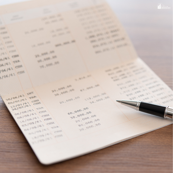An open bank passbook with printed transaction records and a pen placed on a wooden table.