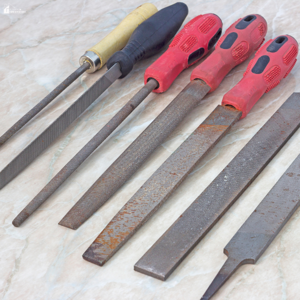 A variety of hand files with different handles laid out on a marble surface, showing the differences in file shapes and textures.