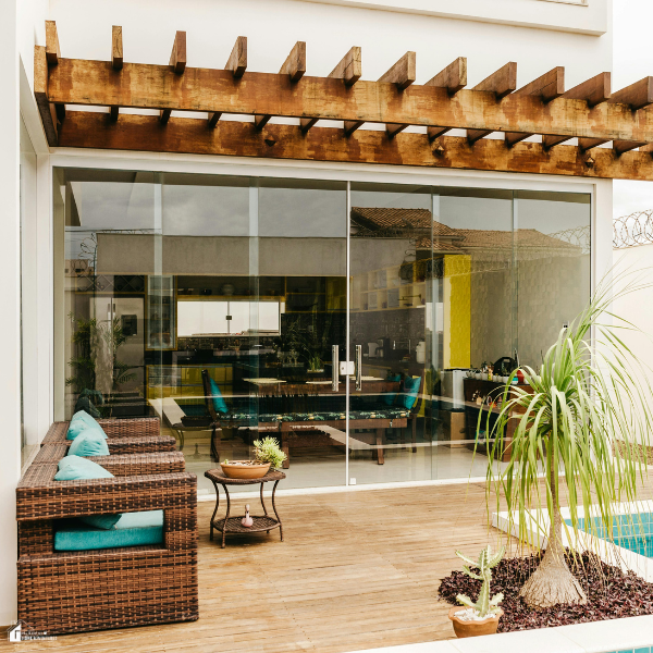 A modern deck with wicker seating, teal cushions, and a wooden pergola above sliding glass doors leading into the home.