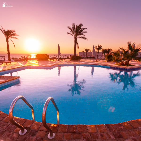 A coastal swimming pool at sunset with palm trees reflecting on the water, showing the impact of saltwater air on outdoor spaces.