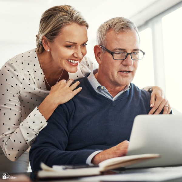 A smiling couple reviews retirement plans together on a laptop at home.