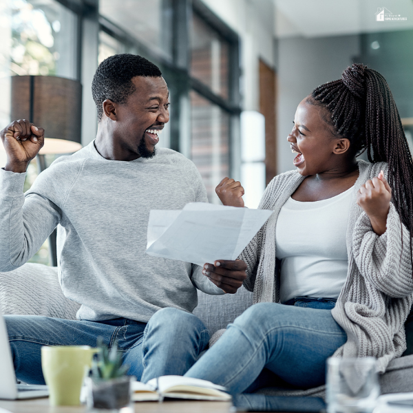 A couple celebrates together at home while holding a document, symbolizing the rewards of patience and perseverance.
