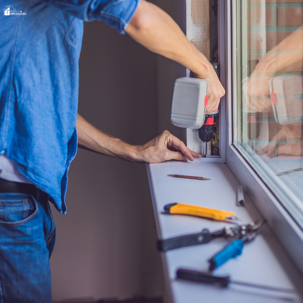 A person uses a power drill to perform maintenance on a window frame in a home interior.