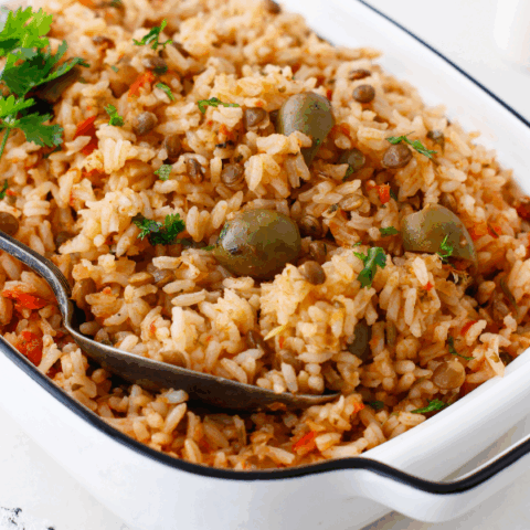 Close-up of seasoned arroz con gandules with visible olives, pigeon peas, and chopped herbs in a white dish.