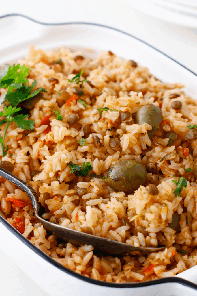 Close-up of seasoned arroz con gandules with visible olives, pigeon peas, and chopped herbs in a white dish.