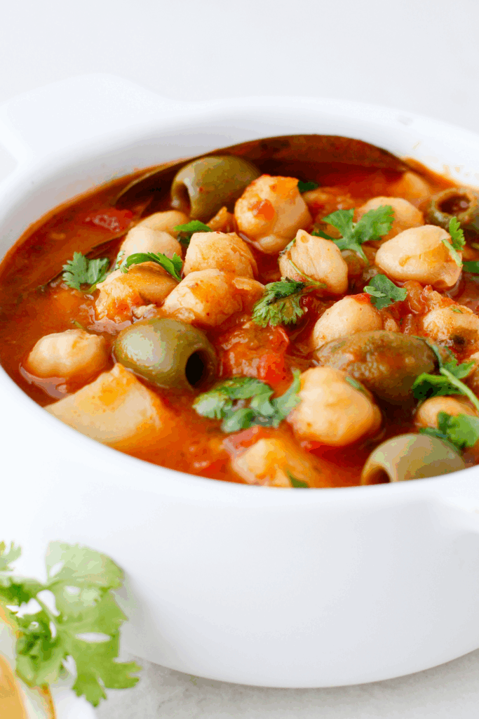 A close-up of Puerto Rican stewed chickpeas simmered in tomato sauce with green olives and fresh cilantro.