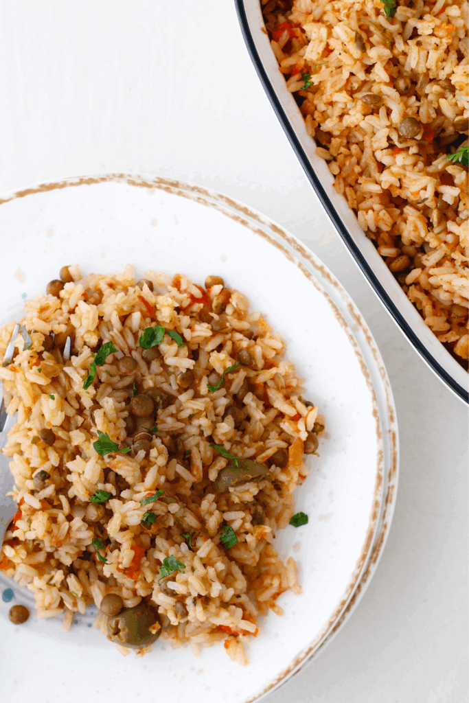 A plated portion of arroz con gandules on a rustic white plate, showing a serving next to the larger dish.