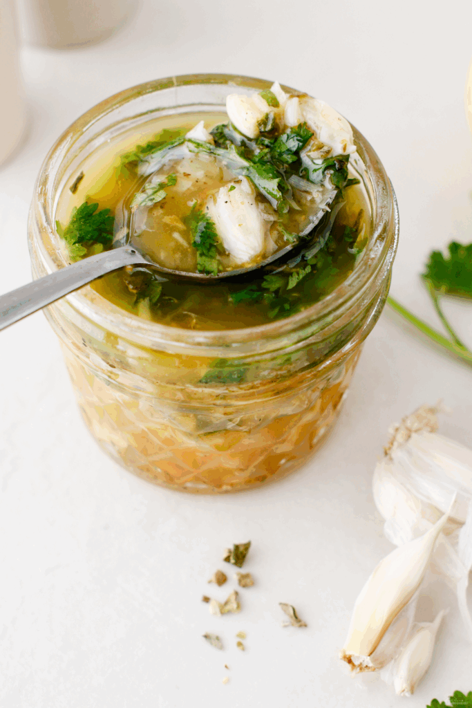 A jar of Puerto Rican mojo sauce with a spoon scooping out the garlicky herb mixture.