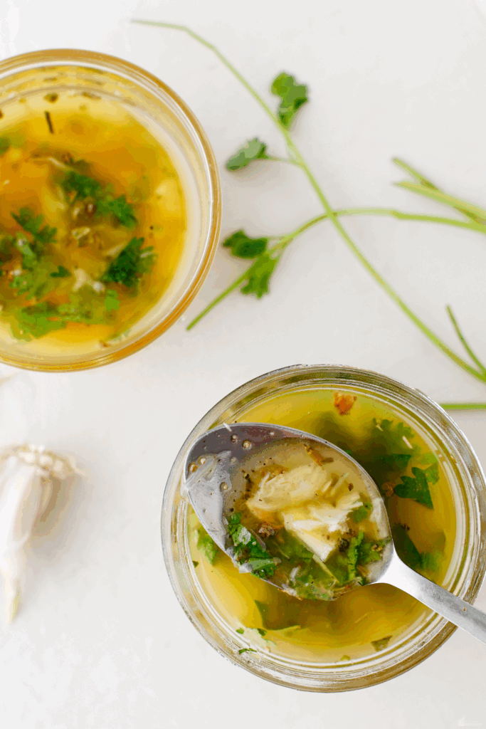 A glass jar filled with Puerto Rican mojo sauce garnished with fresh cilantro and garlic.