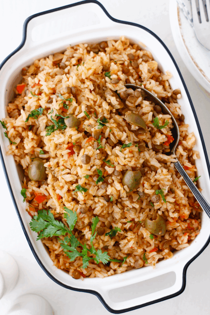 A serving dish filled with Puerto Rican arroz con gandules, garnished with fresh cilantro and green olives.