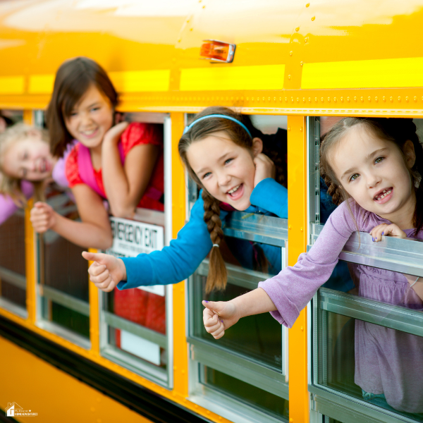 A group of smiling children lean out of a bright yellow school bus window with thumbs up, ready for the first day of school.