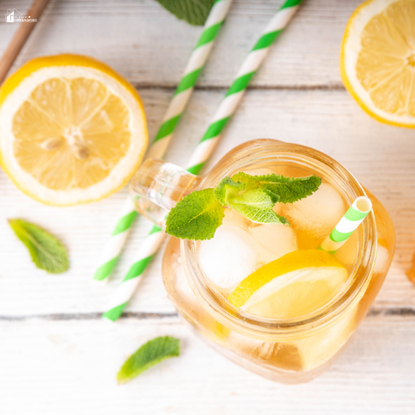 A refreshing lemon drink in a mason jar with ice, mint leaves, and striped green paper straws.