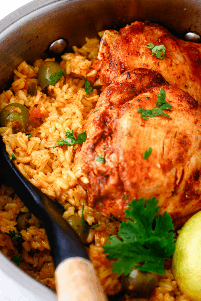 Close-up of cooked arroz con pollo in a pot with seasoned chicken thighs nestled in fluffy, flavorful rice with green olives.