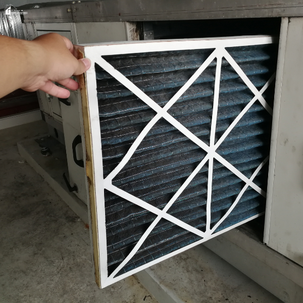 A person removes a used HVAC furnace filter from a metal unit in a garage.
