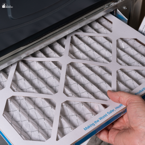 A clean pleated furnace filter is being installed into a residential HVAC system.