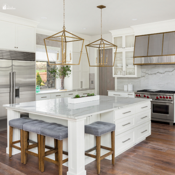 Elegant white kitchen with gold pendant lights, marble countertops, and a spacious island with gray upholstered stools.