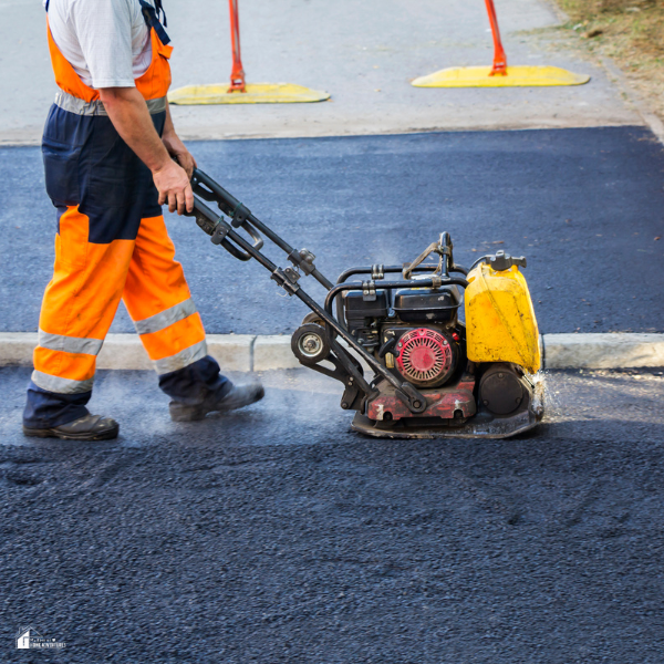 A road worker uses a plate compactor to smooth and compress newly laid asphalt.