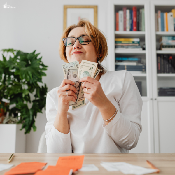A woman sits at a desk holding cash with a joyful expression, representing financial readiness.