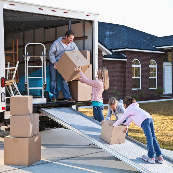 A family loads cardboard boxes into a moving truck outside their suburban home during a relocation.