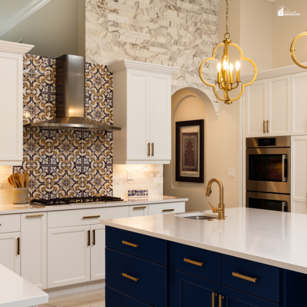 A luxury kitchen featuring white cabinets, a white island with navy drawers, and a detailed terracotta tile backsplash behind the stove.