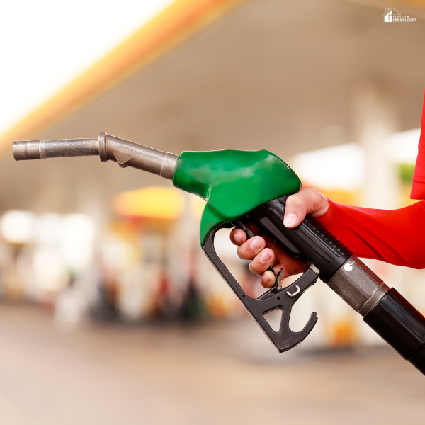 A hand holding a green fuel nozzle at a gas station with blurred background.