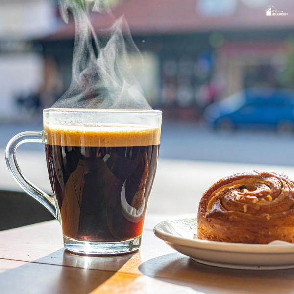 A steaming glass of coffee next to a pastry on a table at a gas station cafe.