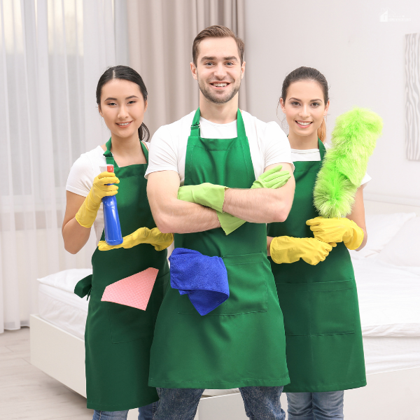 Three cleaning professionals in green aprons stand confidently with cleaning tools.