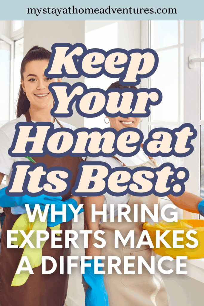 Two cleaning home experts wearing aprons and cleaning gloves stand by a bright window holding cleaning supplies.