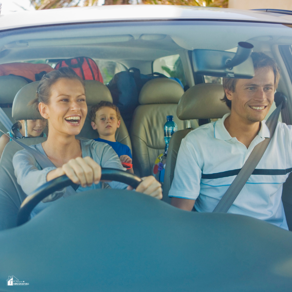 A smiling family with children rides in a packed car during a road trip or move.