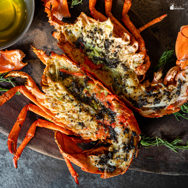 Grilled lobster halves seasoned with herbs and spices served on a wooden platter.