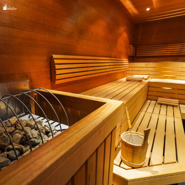A cozy home sauna with wooden benches, a heater filled with stones, and a wooden water bucket.