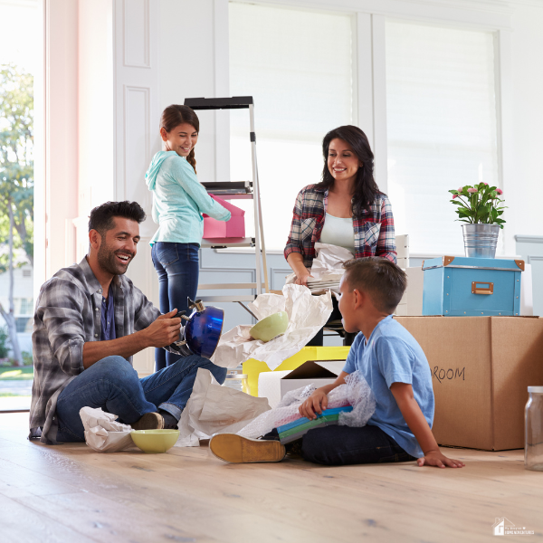 A family of four happily unpacks moving boxes together in a bright living room.