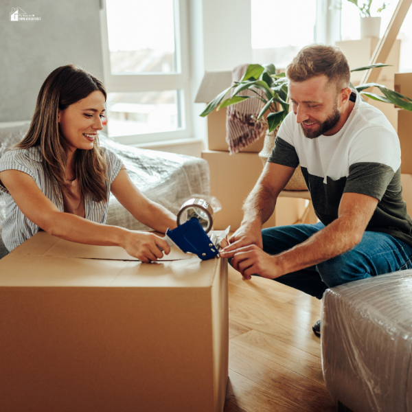 A couple works together sealing a cardboard box while preparing to move into a new home.