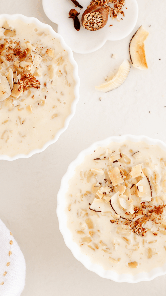 Two white bowls filled with creamy coquito oatmeal topped with toasted coconut flakes and warm spices on a light background.