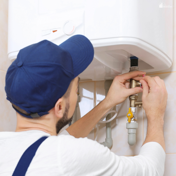 A technician in a blue cap adjusts a valve underneath a wall-mounted water heater unit.