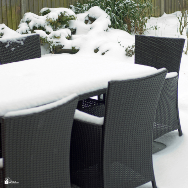 Outdoor wicker dining furniture covered in a thick layer of snow in a backyard during winter.