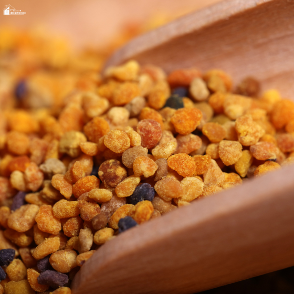 A wooden spoon holds colorful granules of bee pollen in various shades of yellow, orange, and brown.