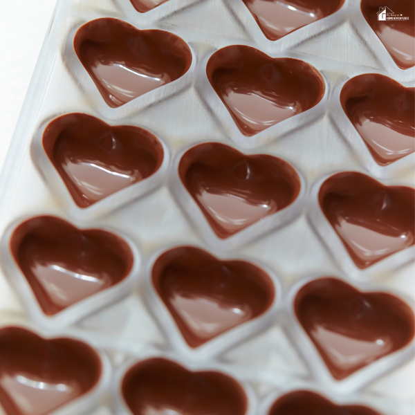 A plastic heart-shaped mold tray filled with melted chocolate on a white surface.
