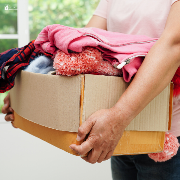 Person holding a cardboard box filled with preloved or gently used kids' clothes.
