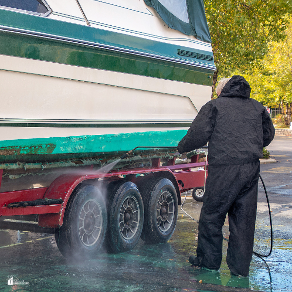 A person power-washes a boat on a trailer as part of essential winter preparation and proper storage maintenance.