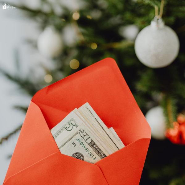 A red envelope filled with cash in front of a Christmas tree symbolizes setting aside money to stay on budget during the expensive holiday season.