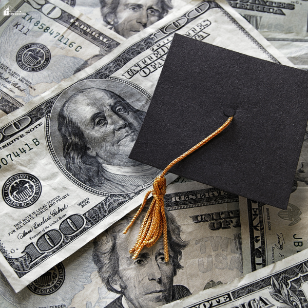A small graduation cap rests on hundred-dollar bills, representing student loans and the cost of college education in 2025.