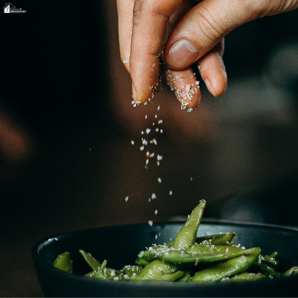 A hand sprinkles seasoning over a bowl of green vegetables, showing how Mediterranean flavors elevate simple dishes.
