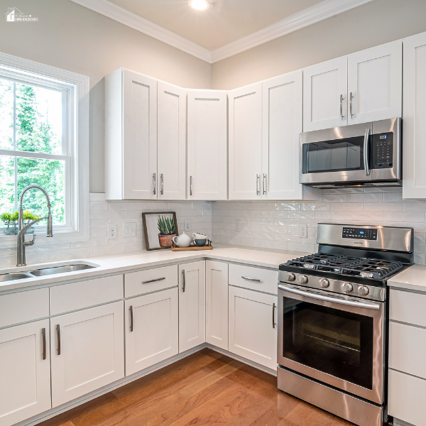 A modern white kitchen featuring sleek cabinets, stainless steel appliances, and a sunlit window by the sink.