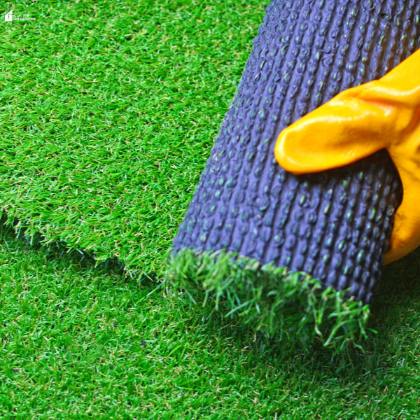 A hand rolls out artificial turf, showing a low-maintenance alternative to natural grass.
