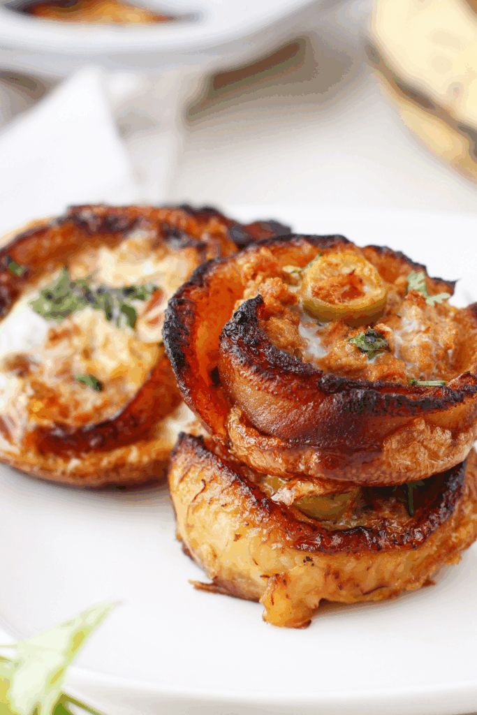 Stack of golden-brown plantain cups on a white plate, showing the crispy edges and savory beef filling inside.