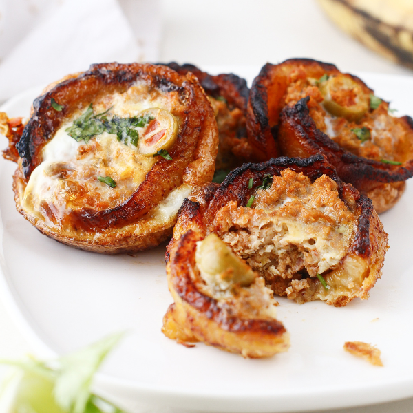 Plate of multiple plantain cups, one partially eaten to reveal the seasoned ground beef and olive filling.
