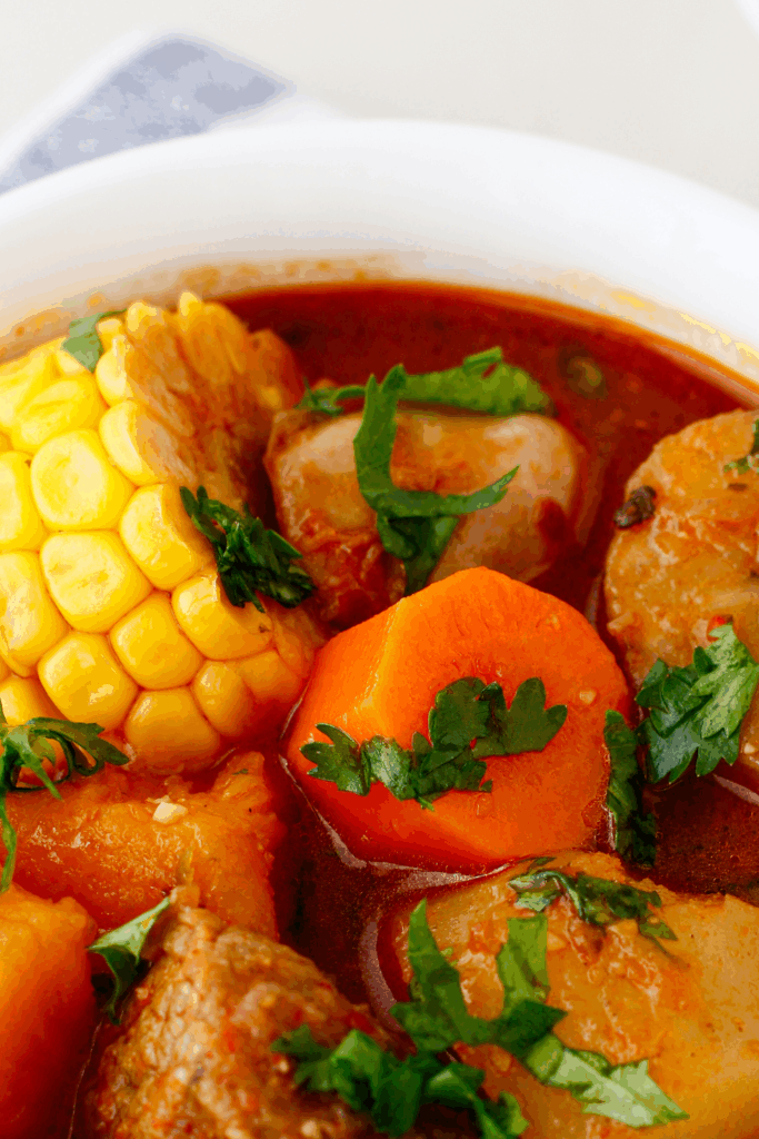 Close-up of beef sancocho showcasing vibrant chunks of corn, carrot, calabaza, and fresh herbs in a flavorful broth.
