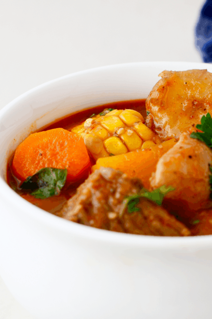 Side angle of a hearty bowl of Puerto Rican beef sancocho stew with visible plantains, root vegetables, and a golden-red broth.