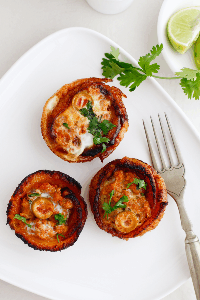 Three baked Puerto Rican Piñonos garnished with cilantro on a white plate next to a fork and lime wedge.